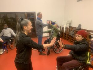 fotografia de duas pessoas em cadeiras de rodas a interagir com dois pessoas em pé, dentro de uma sala.